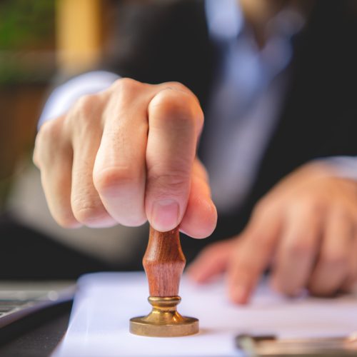 person's hand stamping with approved stamp on approval certificate document